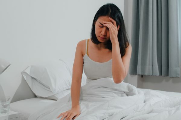 Jovem na cama com pijama sentindo dor de cabeça.